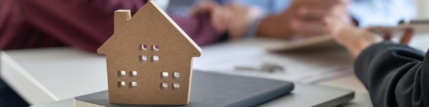 wooden house sitting on top of a folder with blurry hands in the background