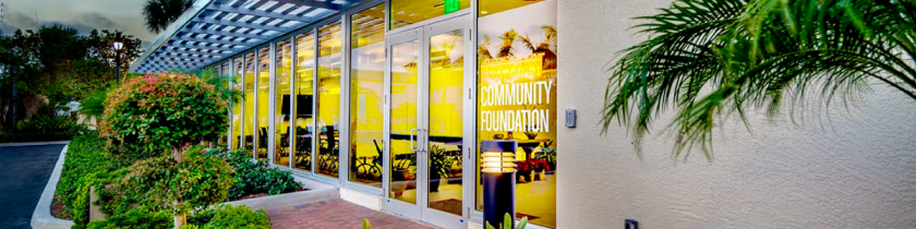 outside of an office building with glass doors and trees and bushes all around the walkway