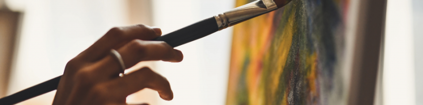 hand holding a black paint brush against a piece of artwork with green and yellow