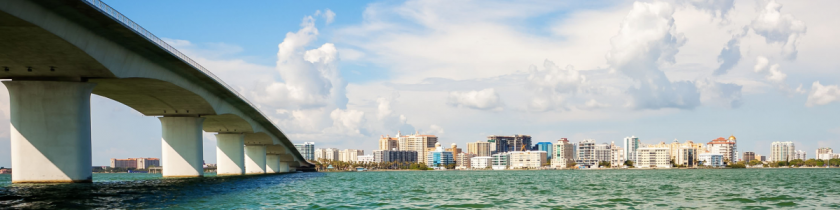 city skyline over blue green water with a bridge going into the city