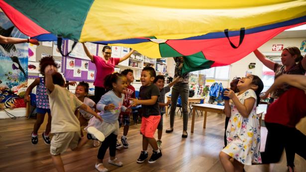 Children jumping, playing under colorful parachute.