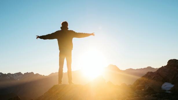 Person standing with arms out overlooking sunrise.