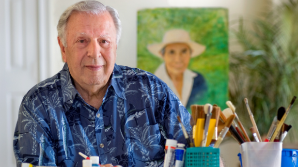 Man sitting at desk smiling with cups filled with paintbrushes.