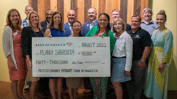 14 people standing, smiling, holding Bank of America large check