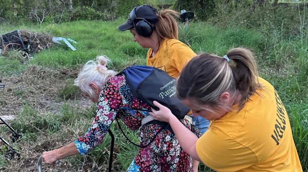 Two volunteers from Shreveport Volunteer Networking help elderly woman with cane.