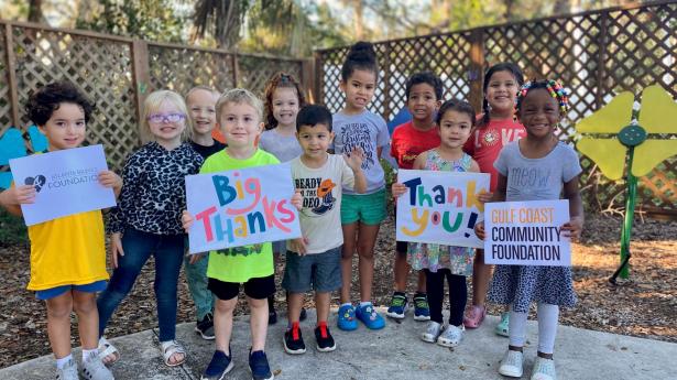 Children from The Florida Center for Early Childhood smile at the camera holding signs that say Gulf Coast Community Foundation, Thank you, Big thanks, and Atlanta Braves Foundation