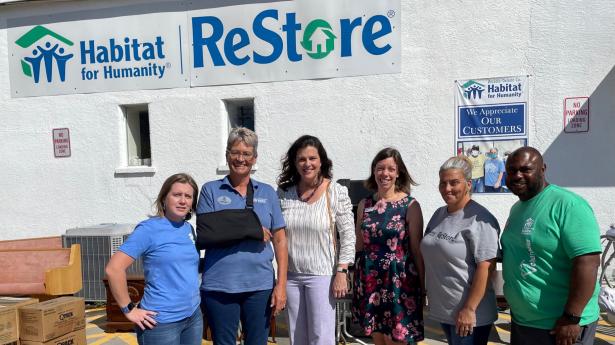 Six people outside standing, smiling at camera. Habitat for Humanity Restore sign and building behind them.