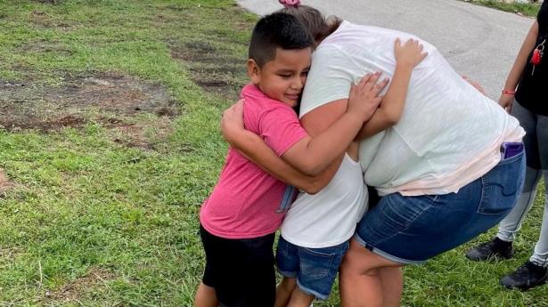 Young boy and another child hug an adult with Hurricane Ian wreckage around them.