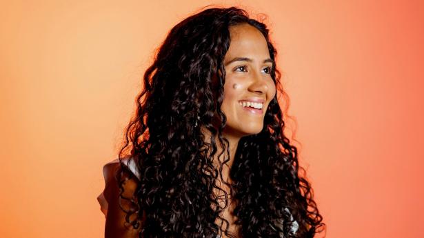 Headshot of visual journalist Karen Arango smiling with long, curly, brown hair.