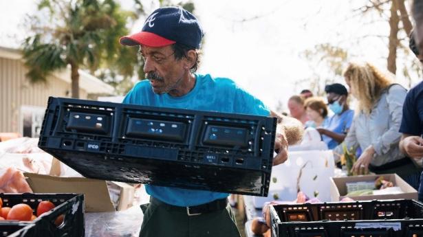 a man stands with baseball cap on carrying a tray of food.