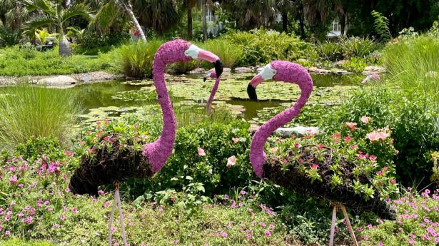 Two crafted flamingos outside among lush forest at Peace River Botanical & Sculpture Gardens.