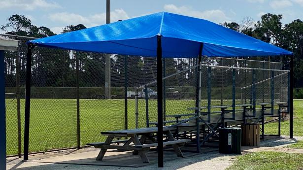 Blue shade structure over picnic tables outside at fields with green grass.