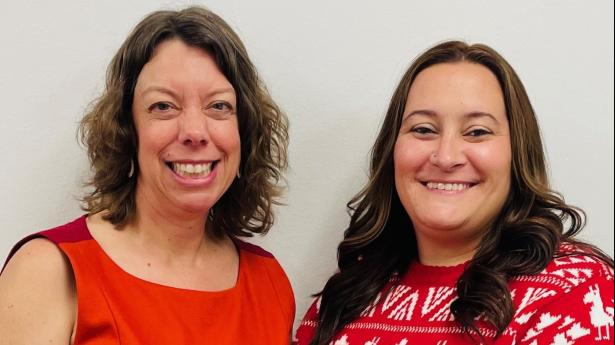 Two brunettes wearing red smile at the camera.