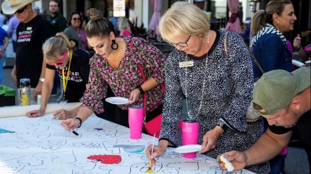 Five people stand outside by white paper painting hearts.