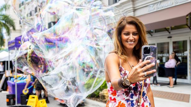 Woman stands outside taking a selfie at Better Together Block Party with big bubbles behind her.