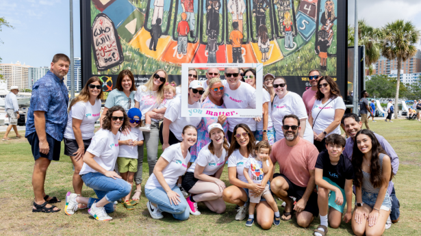 About 15 people smile in front of a large art display with a selfie frame that says You Matter.