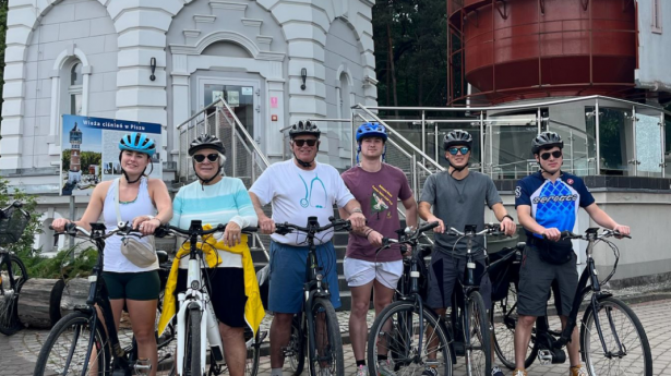 six people on bikes outside a big tower smiling at the camera