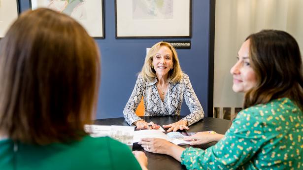 woman smiling at two other when across a black table with papers on it
