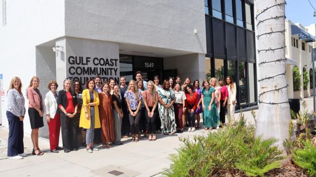 group of people standing outside in front of a concrete building that says Gulf Coast Community Foundation with a tree and bushes next to them