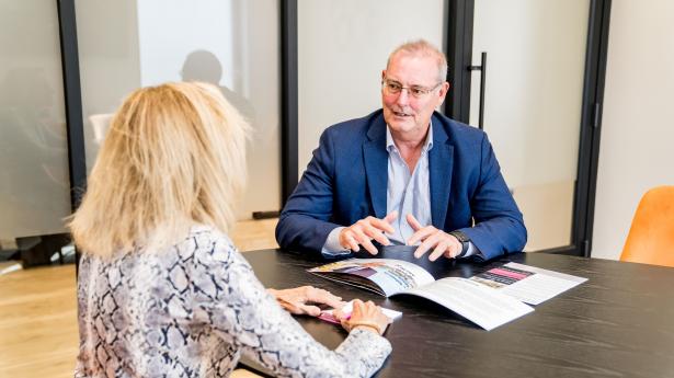 man in a navy jacket talks to a woman across the table wearing a black and white print dress