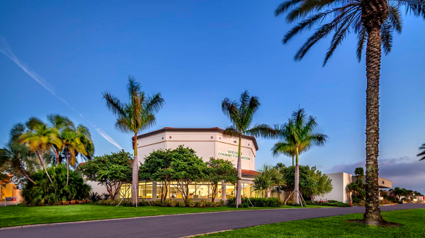 outside of a building with palm trees surrounding it and a blue sky above