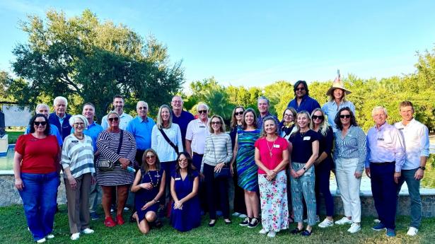 group of 20 people standing outside in the grass with trees behind them smiling
