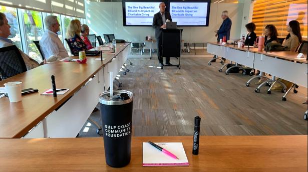 man stands in front of a classroom set up with a cup, pen, and notepad on the table