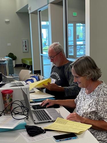 Two people sitting at computers with paperwork.