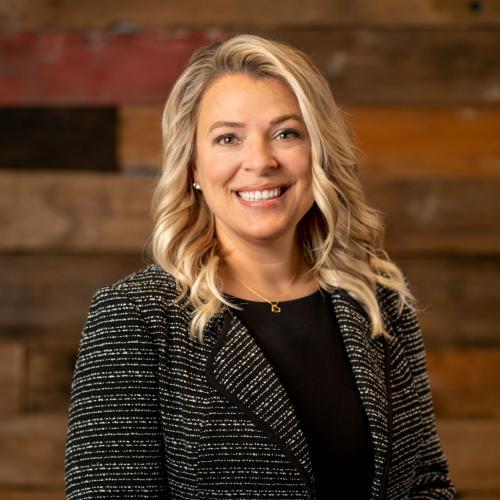 One woman smiles in front of wood wall with black suit.