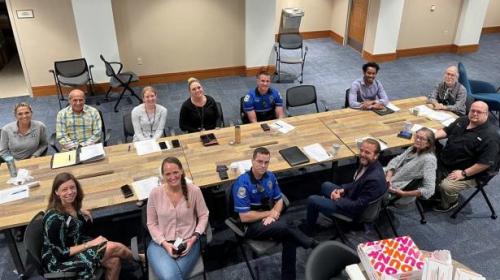 Over 10 people sitting around a table smiling up at camera.