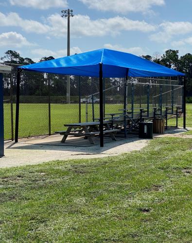 Blue shade structure over picnic tables at fields outdoors with grass.