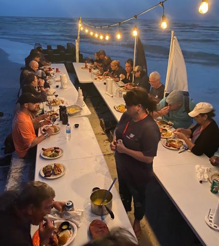 People eating dinner at tables on beach.