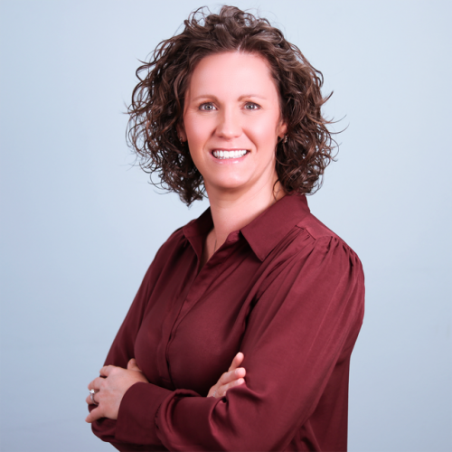 Woman stands with arms crossed, smiling at camera.