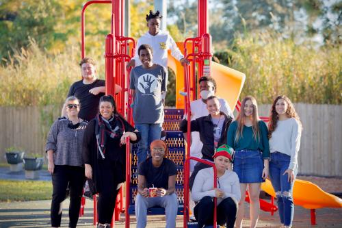 11 people smile at camera around playground outside.