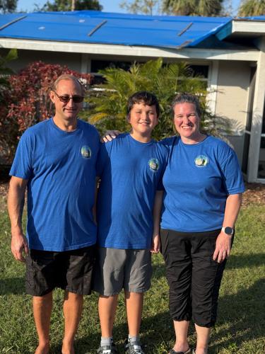 Three people stand in blue t-shirts outside of home.