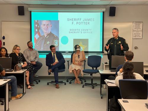 DeSoto County Sheriff stands, speaking to students. Other adults are sitting near him.