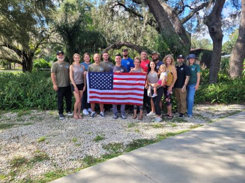 About 10 people stand outside holding U.S. flag.