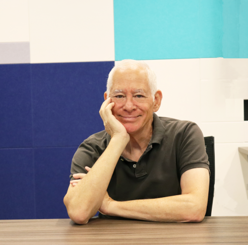 Man sits at table with hand cupped around his face smiling.