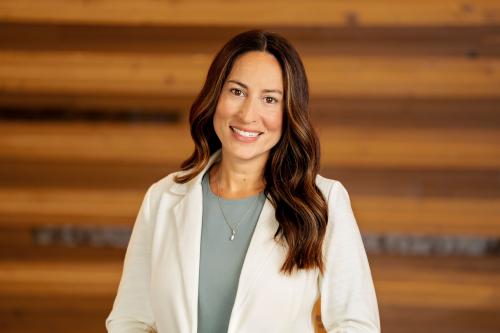 One woman smiles at camera with long brown hair, white jacket, and light blue shirt.