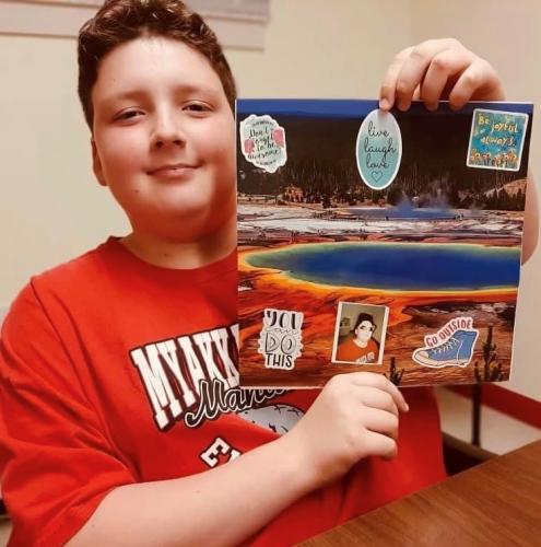 Young boy holds up a collage he decorated that represents where he is in his grief journey.