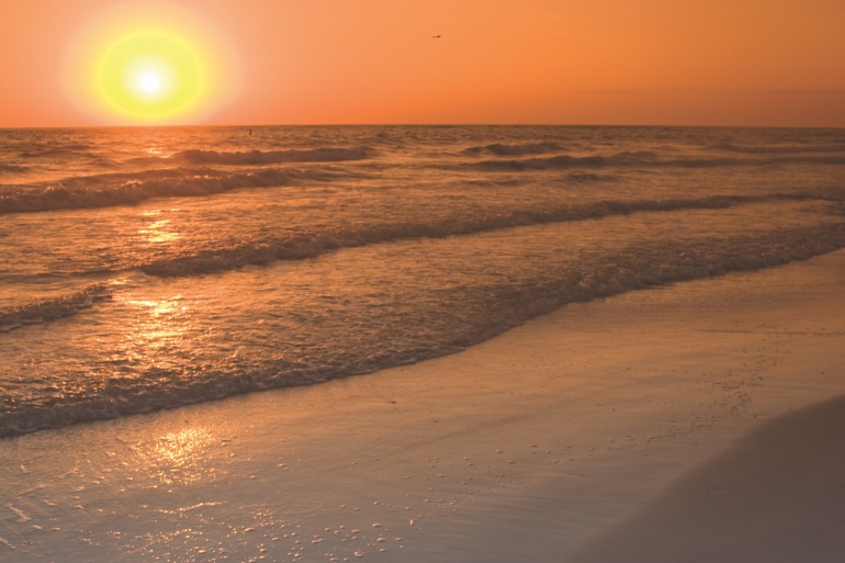 Waves gently crashing with an orange sunset on the horizon