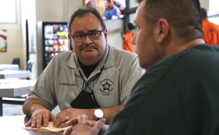 One man from Sarasota County Sheriff's Office smiles at another man in jail.