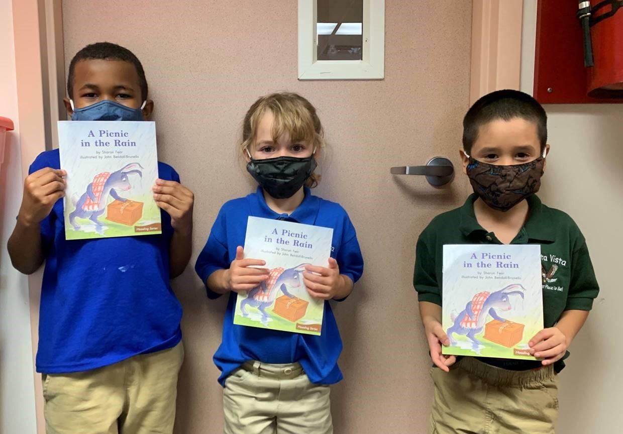 Three students holding books with masks on