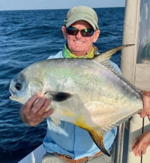 a man holds a large fish on the ocean. He is wearing a hat and sunglasses