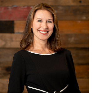 woman smiling in a black and white dress against a wood wall