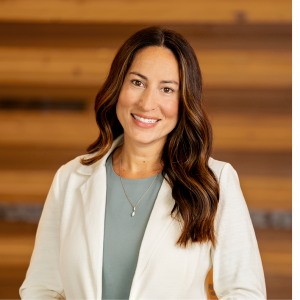 woman smiling in a white jacket against a wood wall